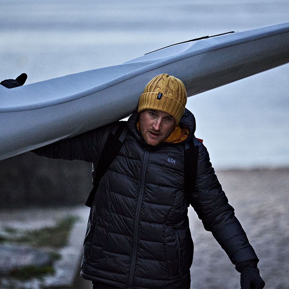 A man wearing a Gill North Hill Jacket and carrying a canoe